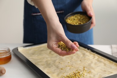 Making delicious baklava. Woman adding chopped nuts to dough at white table, closeup