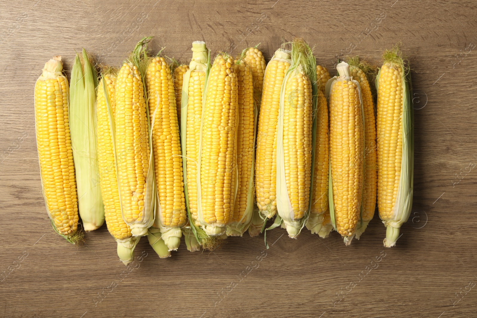 Photo of Tasty sweet corn cobs on wooden table, flat lay