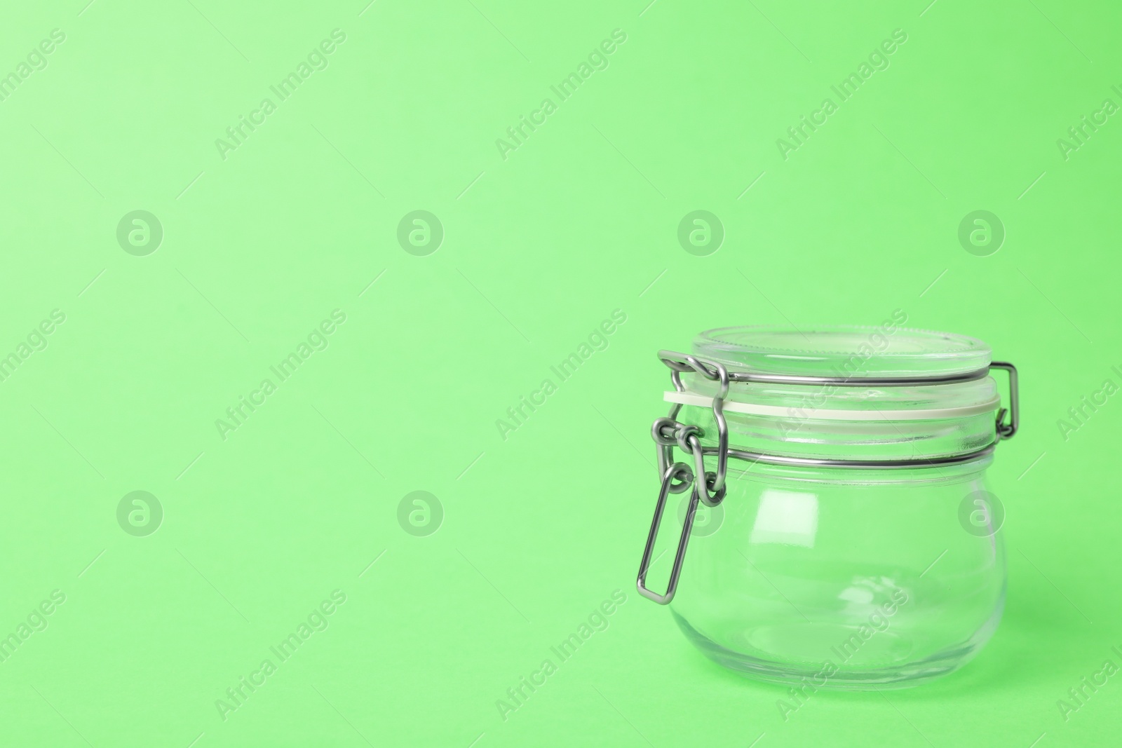 Photo of Closed empty glass jar on light green background, space for text