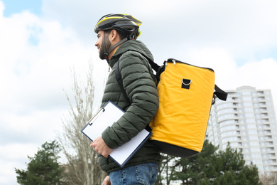 Photo of Courier with thermo bag and clipboard on city street. Food delivery service