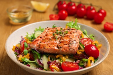 Photo of Bowl with tasty salmon and mixed vegetables on wooden table, closeup