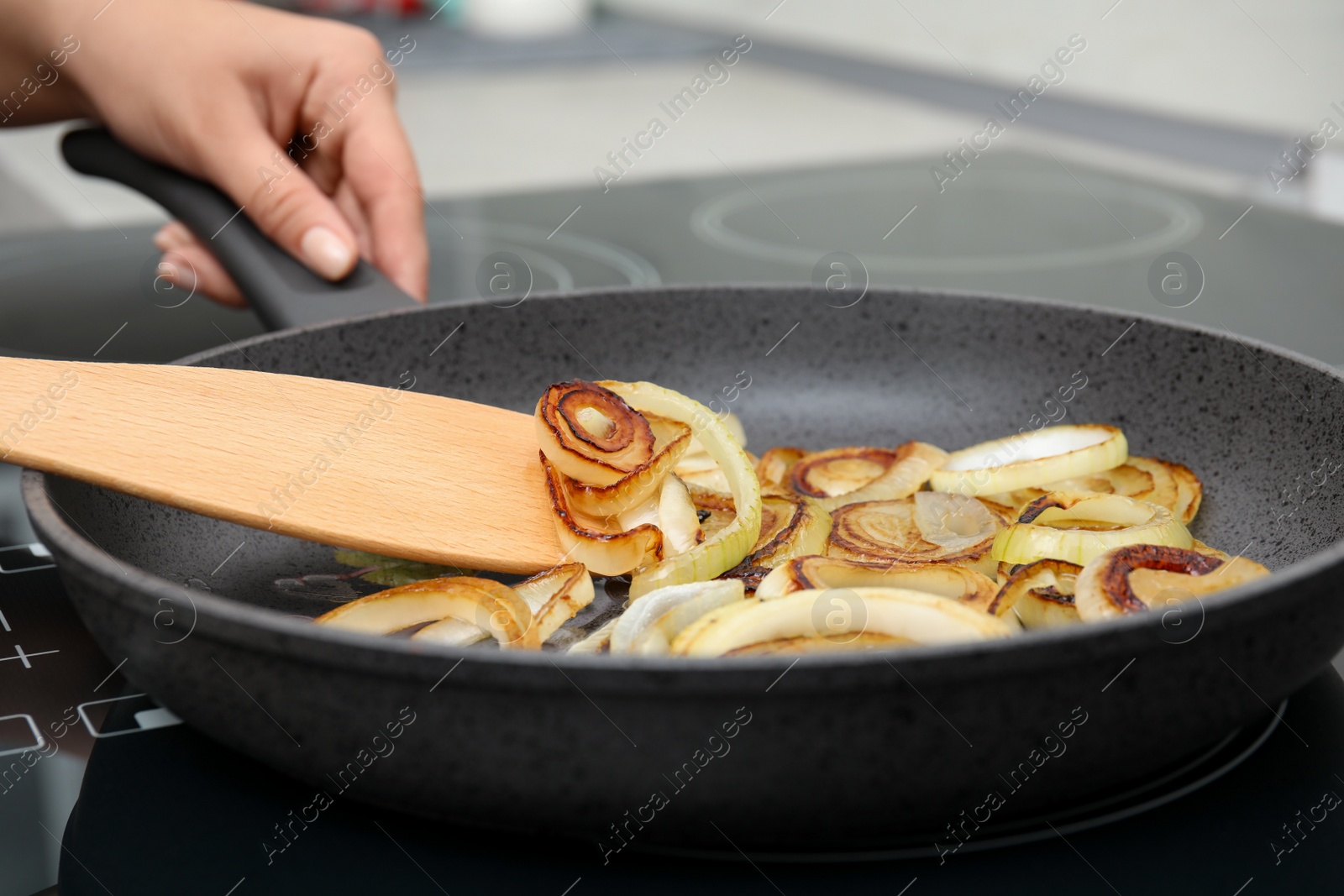 Photo of Woman cooking onion rings in frying pan on stove, closeup