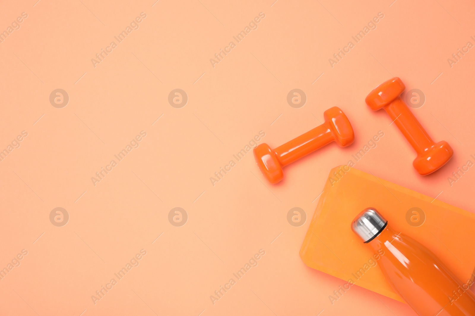 Photo of Dumbbells, thermo bottle and yoga block on coral background, flat lay. Space for text