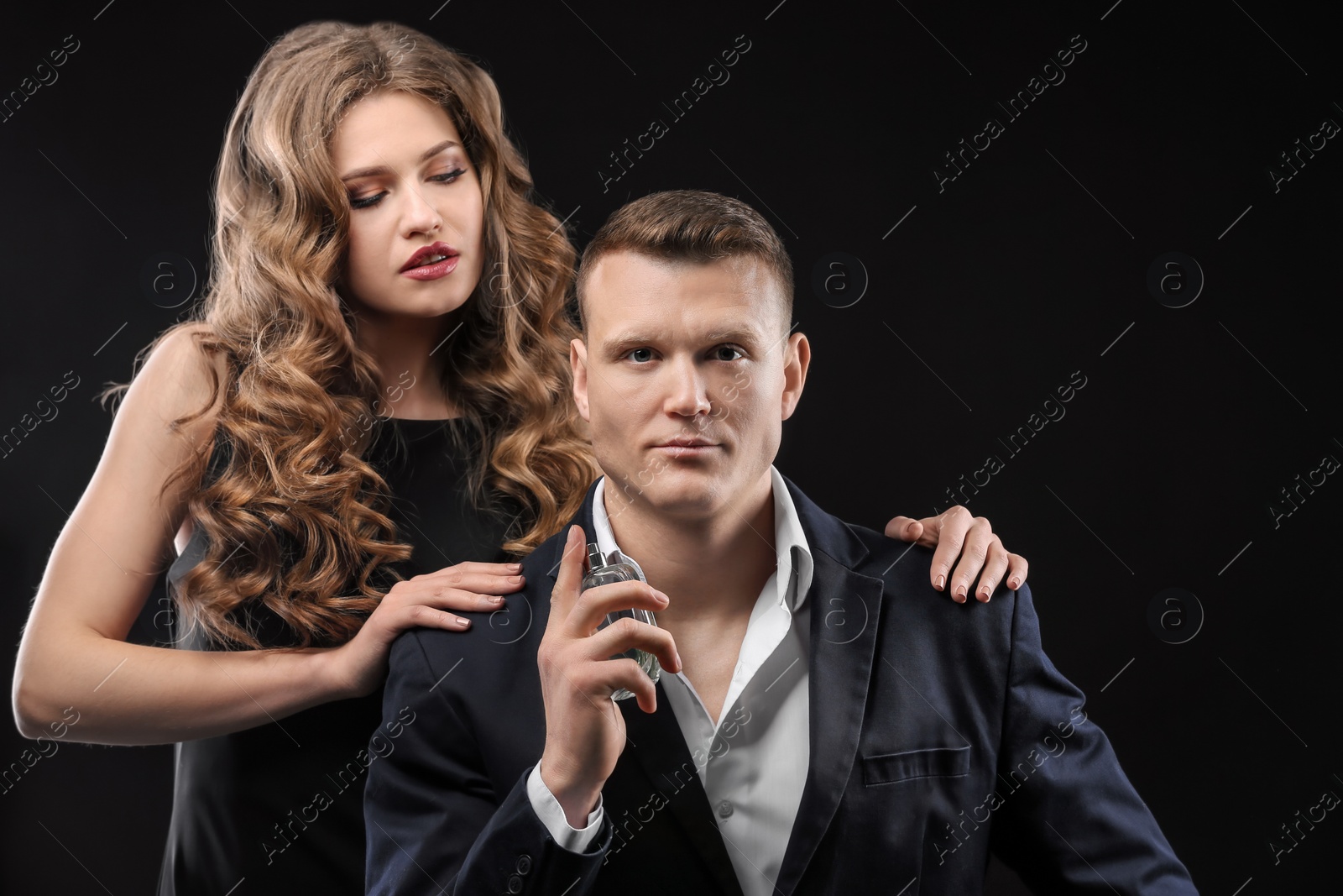 Photo of Passionate woman and handsome man using perfume on black background