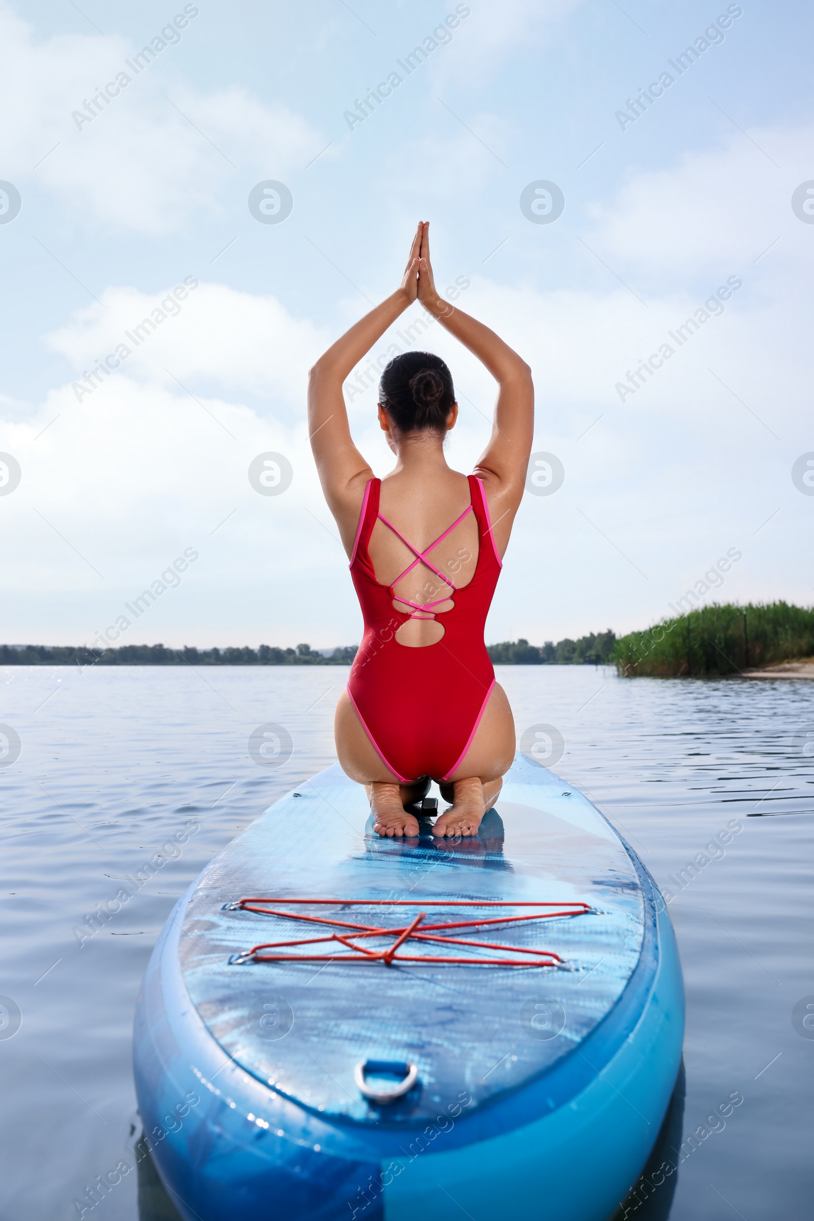 Photo of Woman practicing yoga on light blue SUP board on river, back view