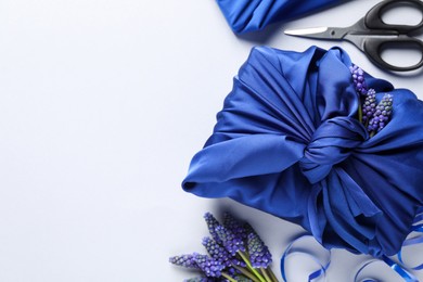 Furoshiki technique. Gifts packed in blue silk fabric, muscari flowers, ribbon and scissors on white table, flat lay. Space for text