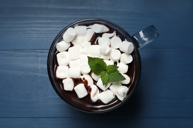 Glass cup of delicious hot chocolate with marshmallows and fresh mint on blue wooden table, top view