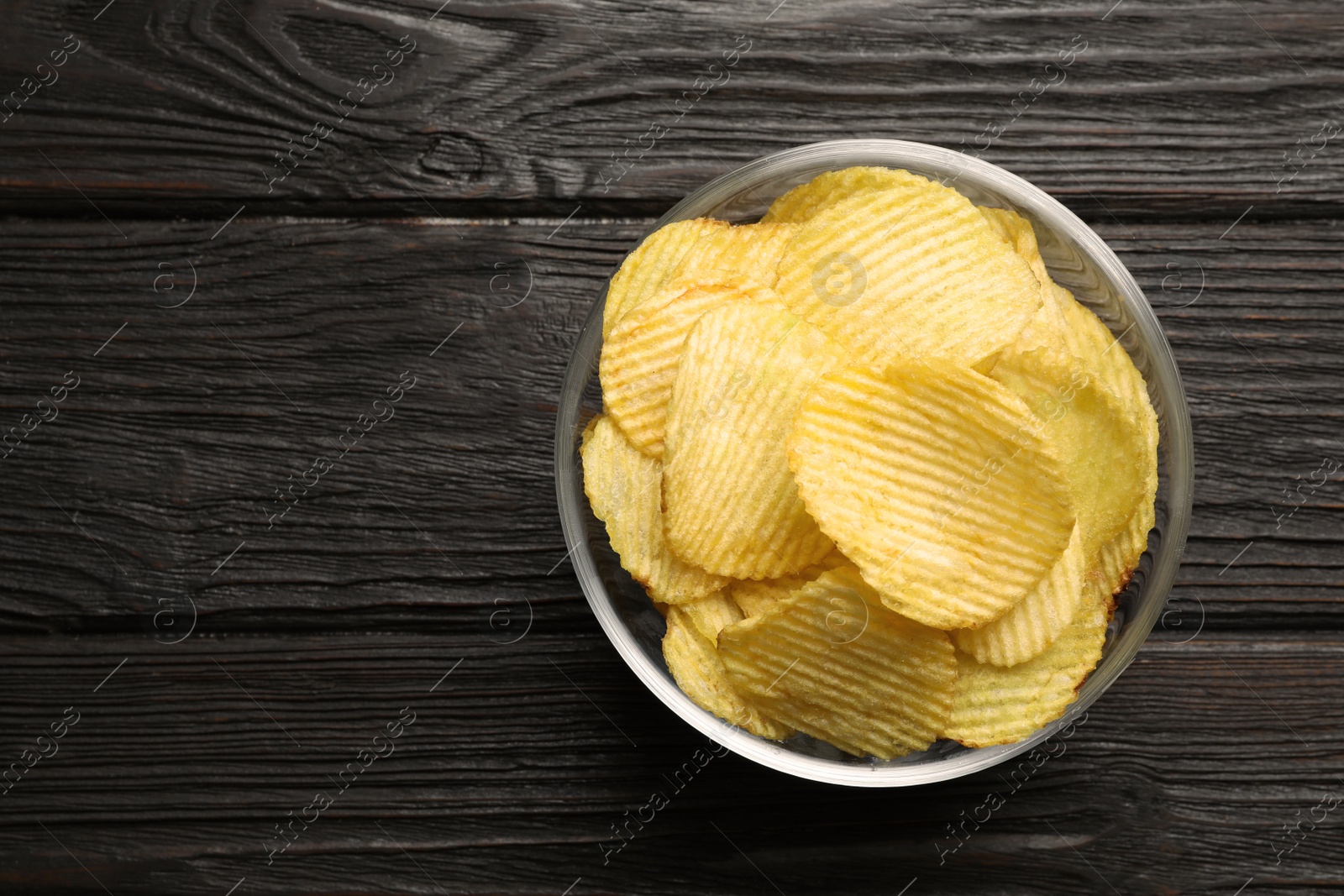 Photo of Bowl of potato chips on wooden table, top view. Space for text