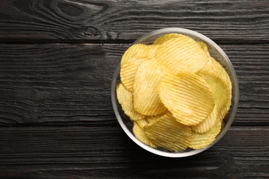 Photo of Bowl of potato chips on wooden table, top view. Space for text