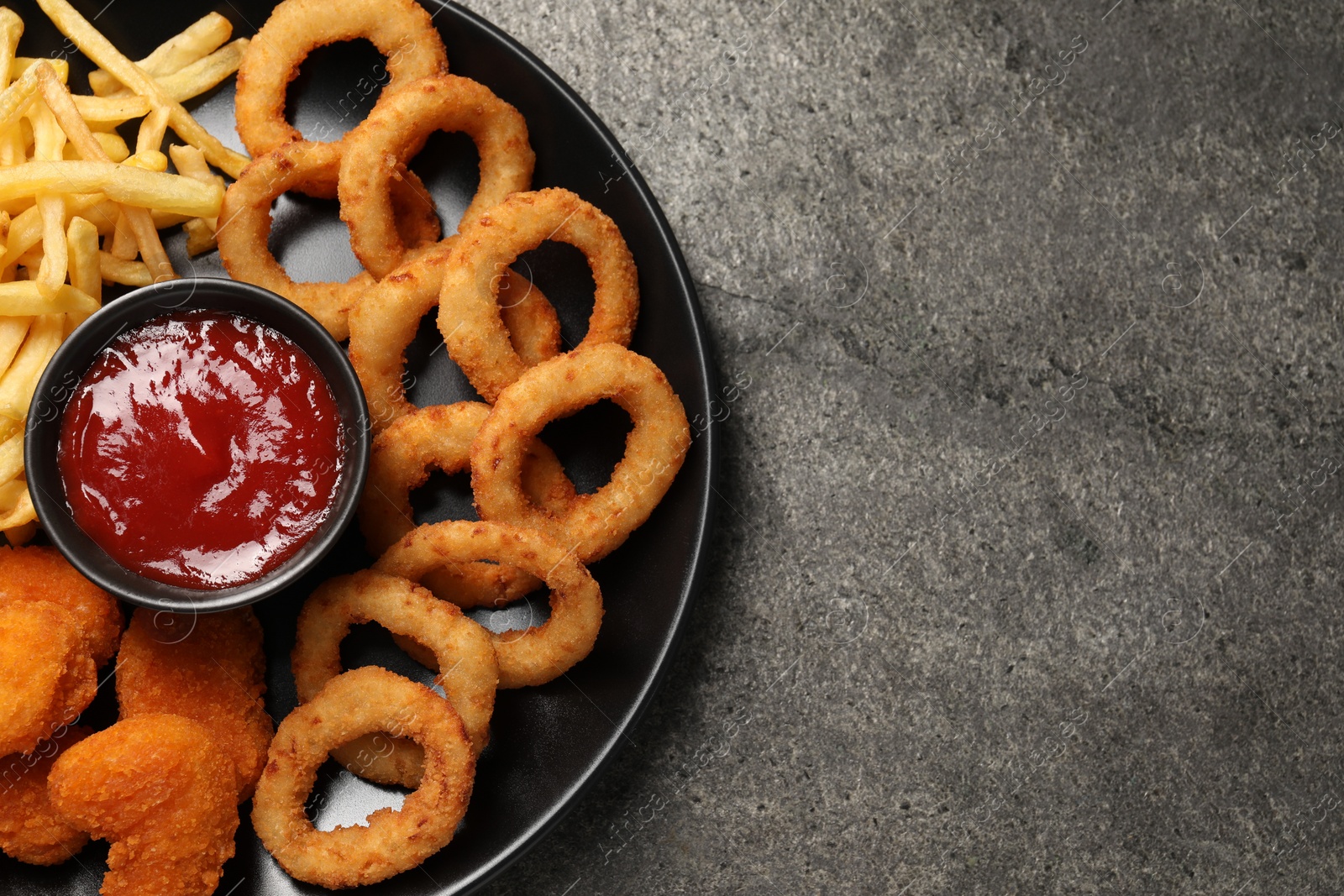 Photo of Plate with tomato ketchup and different snacks on grey textured table, top view. Space for text