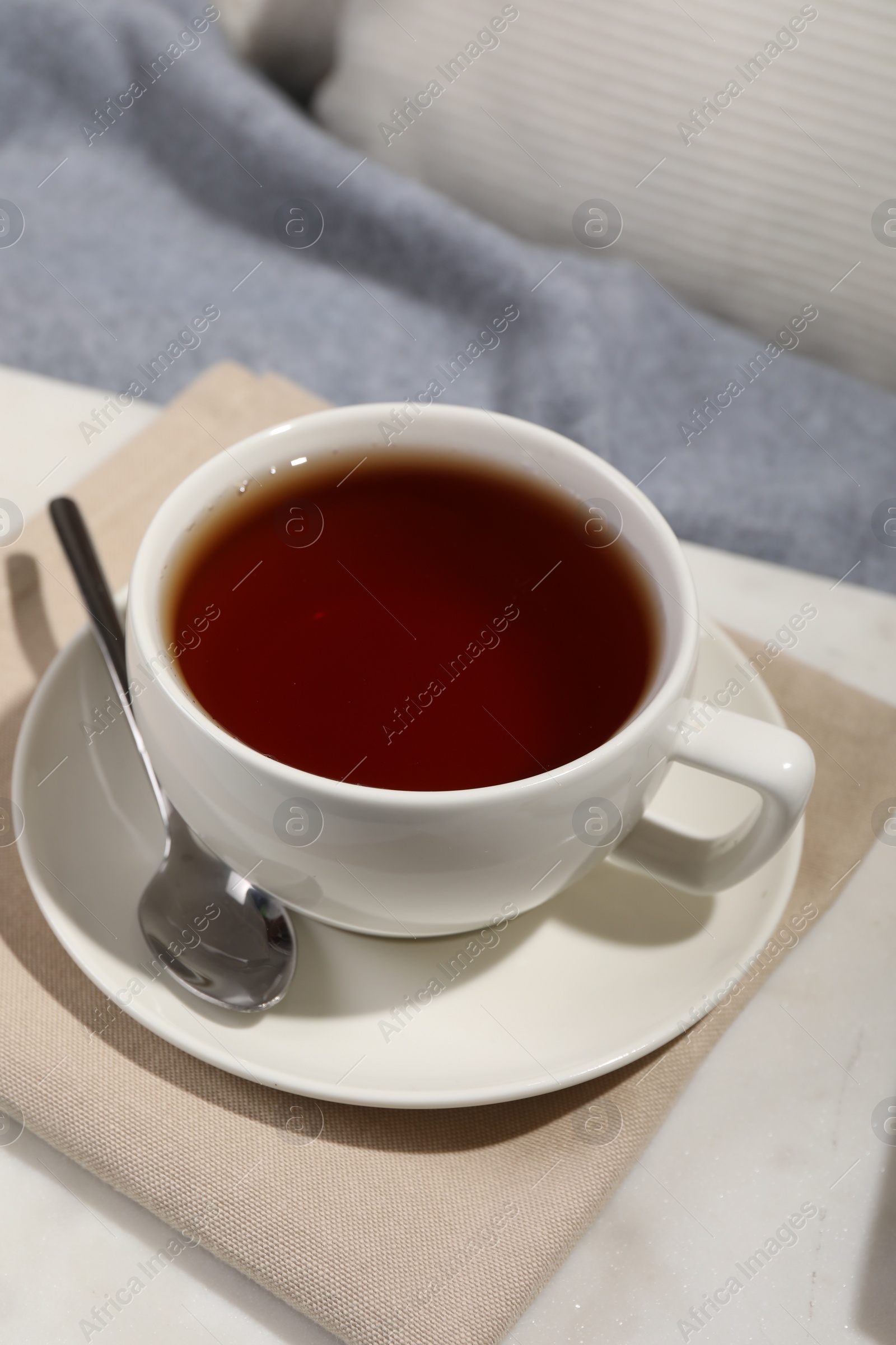 Photo of Aromatic tea in cup, saucer and spoon on table
