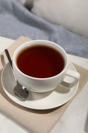 Aromatic tea in cup, saucer and spoon on table