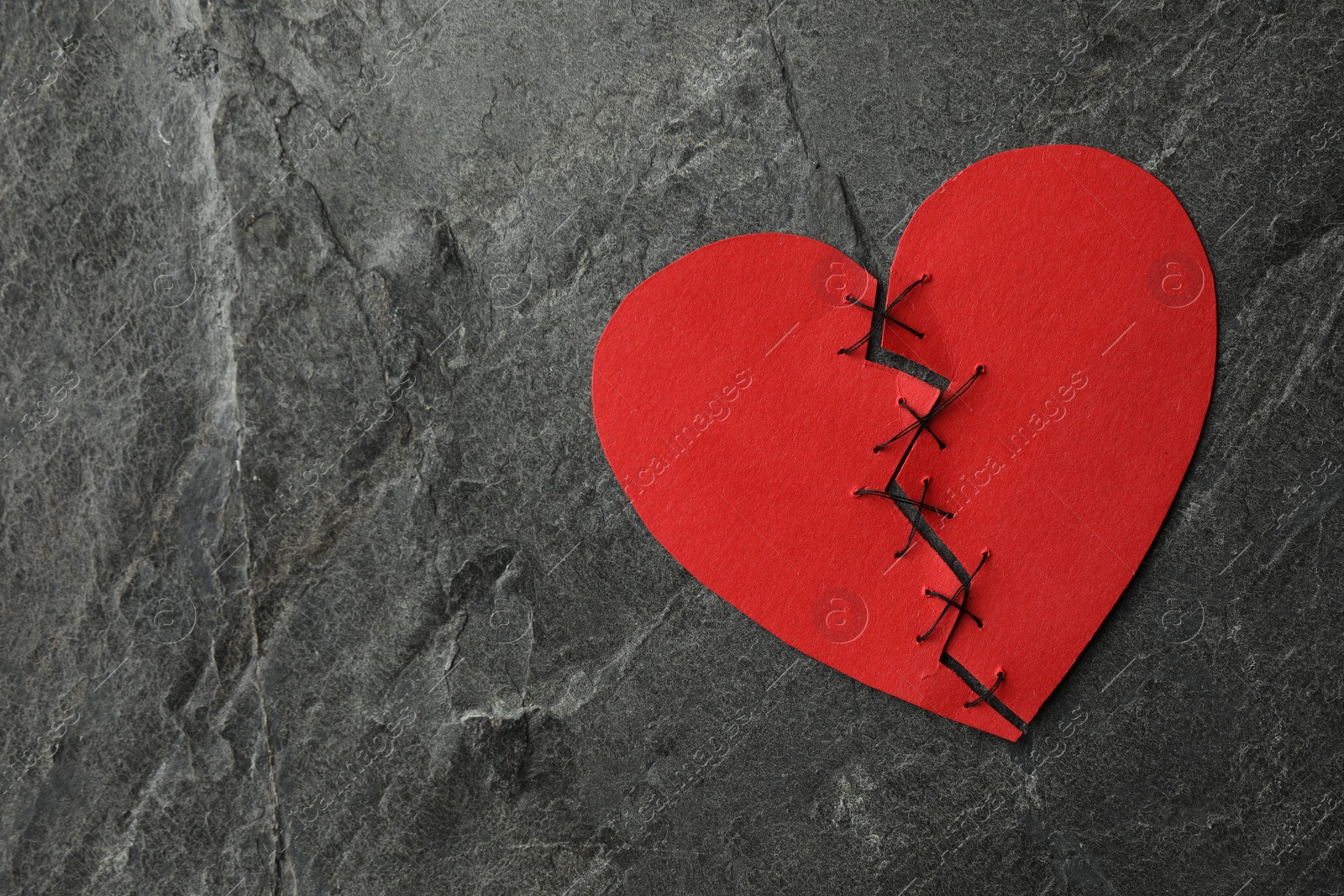 Photo of Broken heart. Torn red paper heart sewed with thread on dark grey table, top view. Space for text