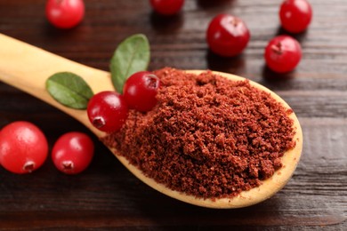 Photo of Dried cranberry powder in spoon, fresh berries and green leaves on wooden table, closeup