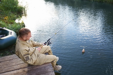 Man with rod fishing on wooden pier at riverside. Recreational activity