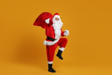 Photo of Santa Claus with bag of Christmas presents posing on orange background