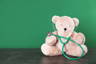 Photo of Toy bear with stethoscope on table against color background, space for text. Children's hospital