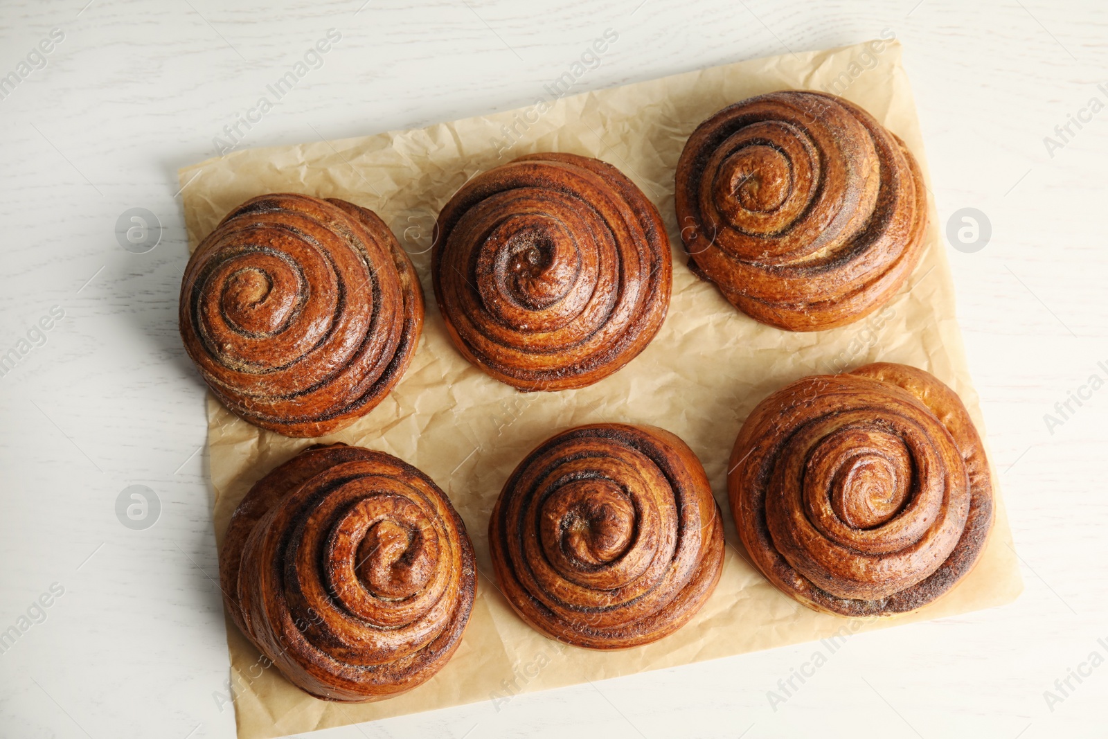 Photo of Parchment with cinnamon rolls on white wooden background, top view