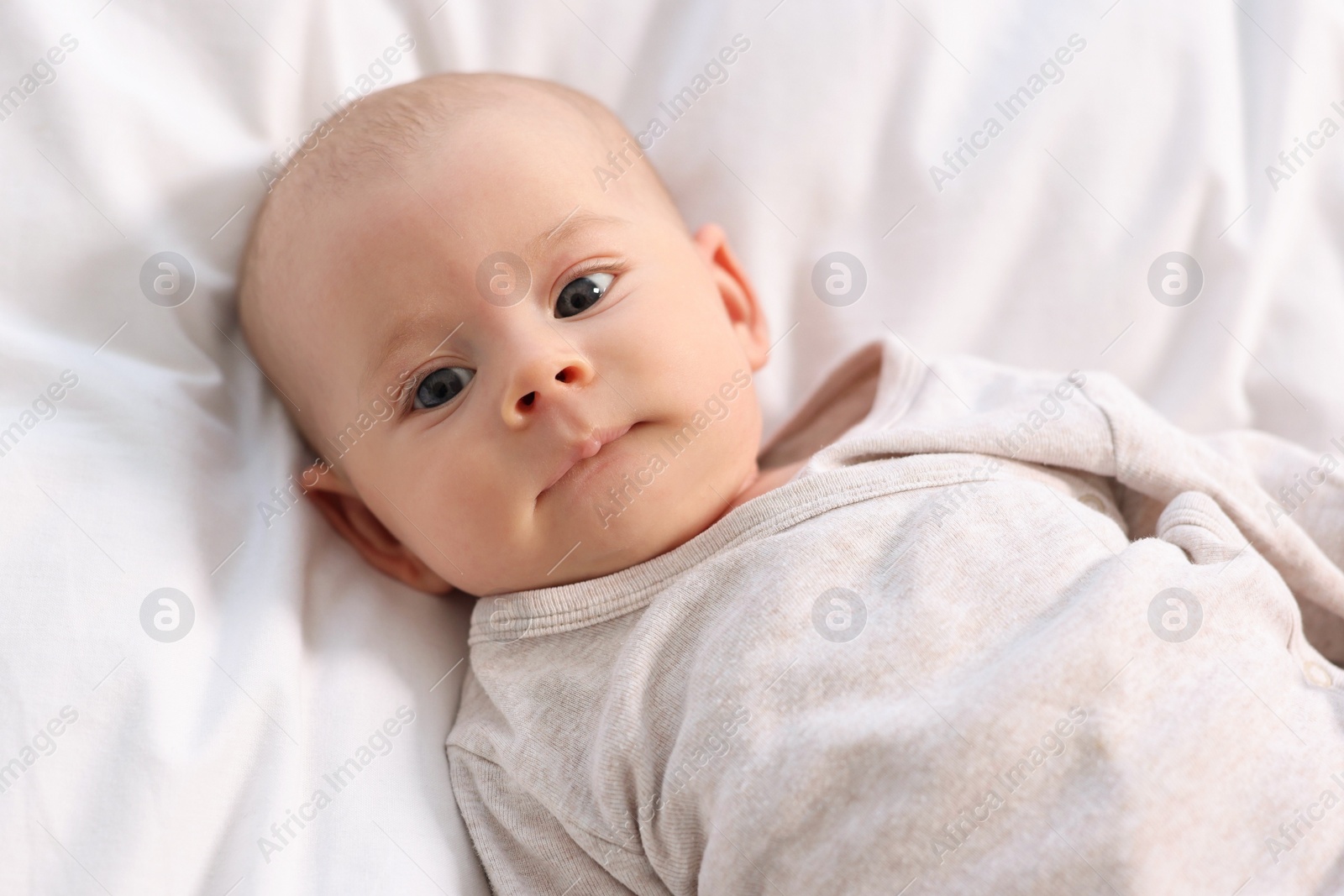 Photo of Cute little baby lying on white sheets, top view