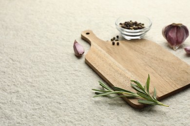 Photo of Cutting board, garlic, pepper and rosemary on white textured table. Space for text