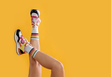Woman wearing stylish sneakers on yellow background, closeup. Space for text