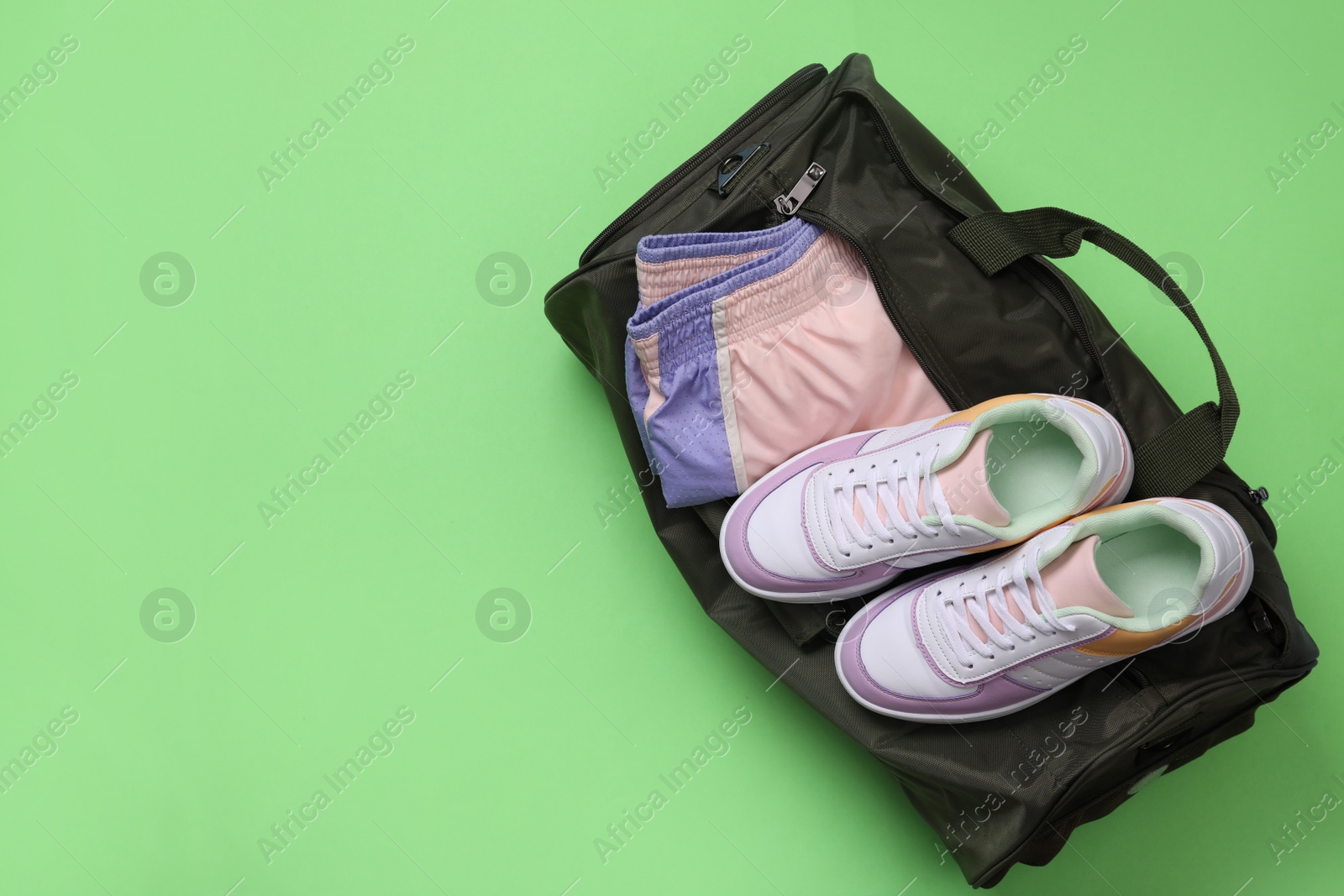 Photo of Sports bag with sneakers and clothes on light green background, top view. Space for text