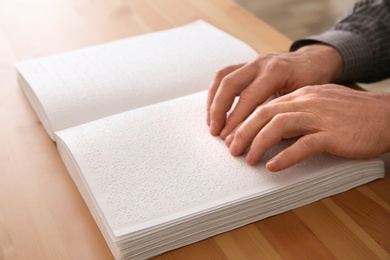 Photo of Blind man reading book written in Braille at table, closeup