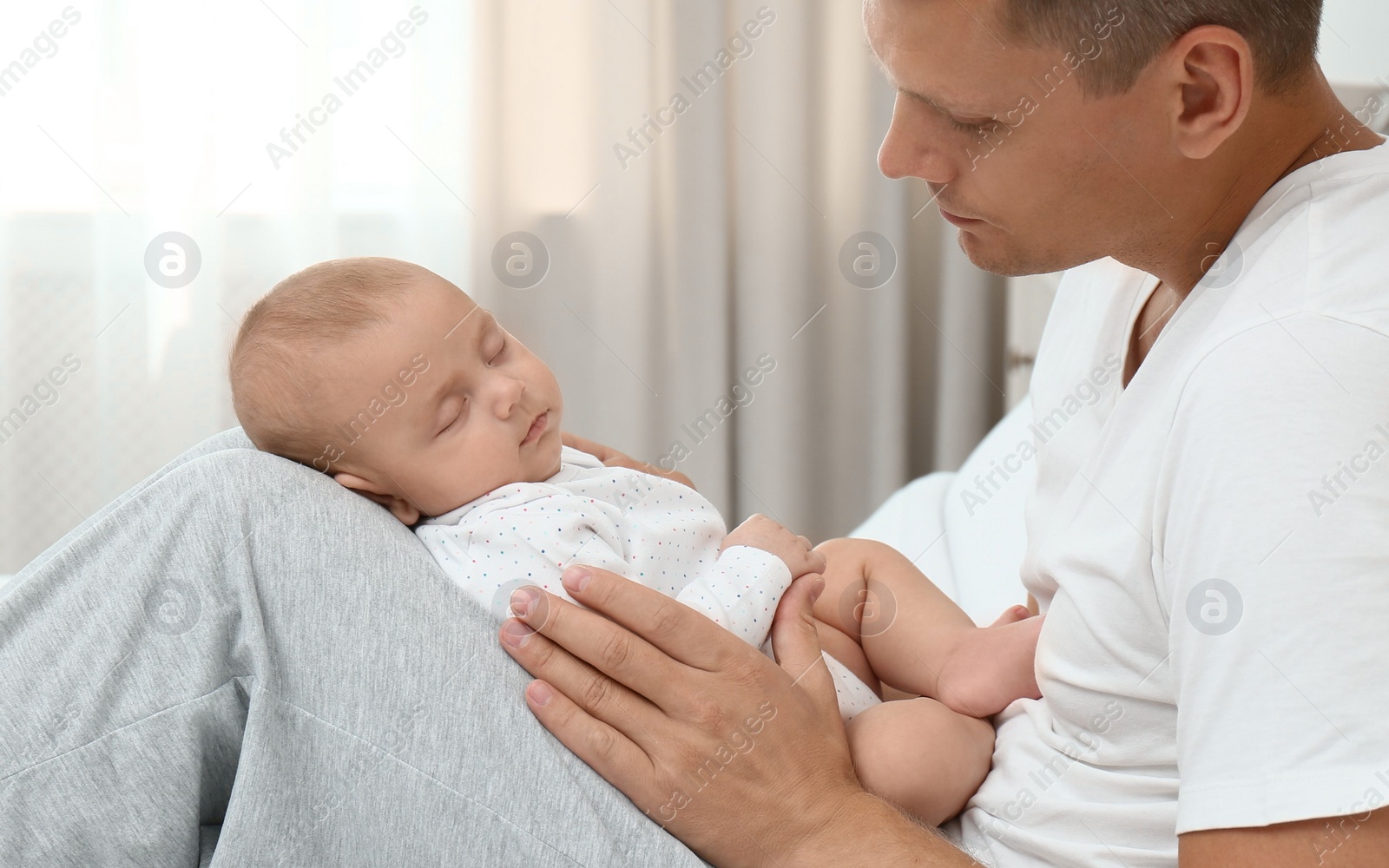 Photo of Happy father holding his cute sleeping baby on bed at home