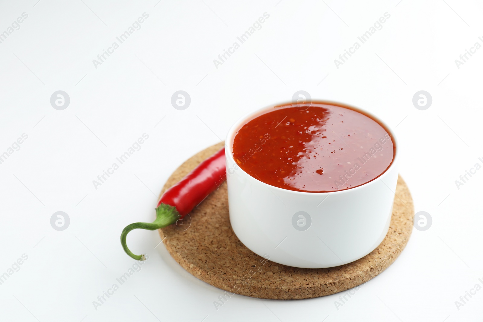 Photo of Spicy chili sauce in bowl and fresh pepper on white background. Space for text