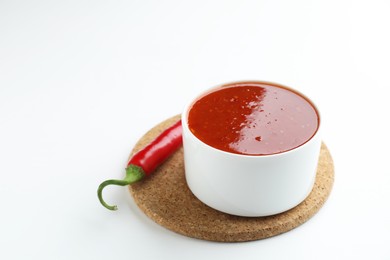 Photo of Spicy chili sauce in bowl and fresh pepper on white background. Space for text