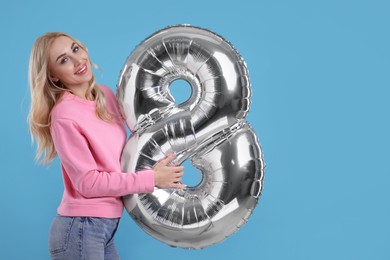 Photo of Happy Women's Day. Charming lady holding balloon in shape of number 8 on light blue background, space for text
