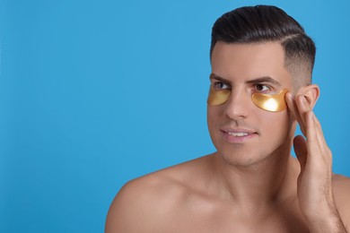 Man applying golden under eye patch on light blue background. Space for text