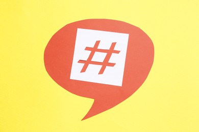 Photo of Red paper speech bubble with hashtag symbol on yellow background, top view