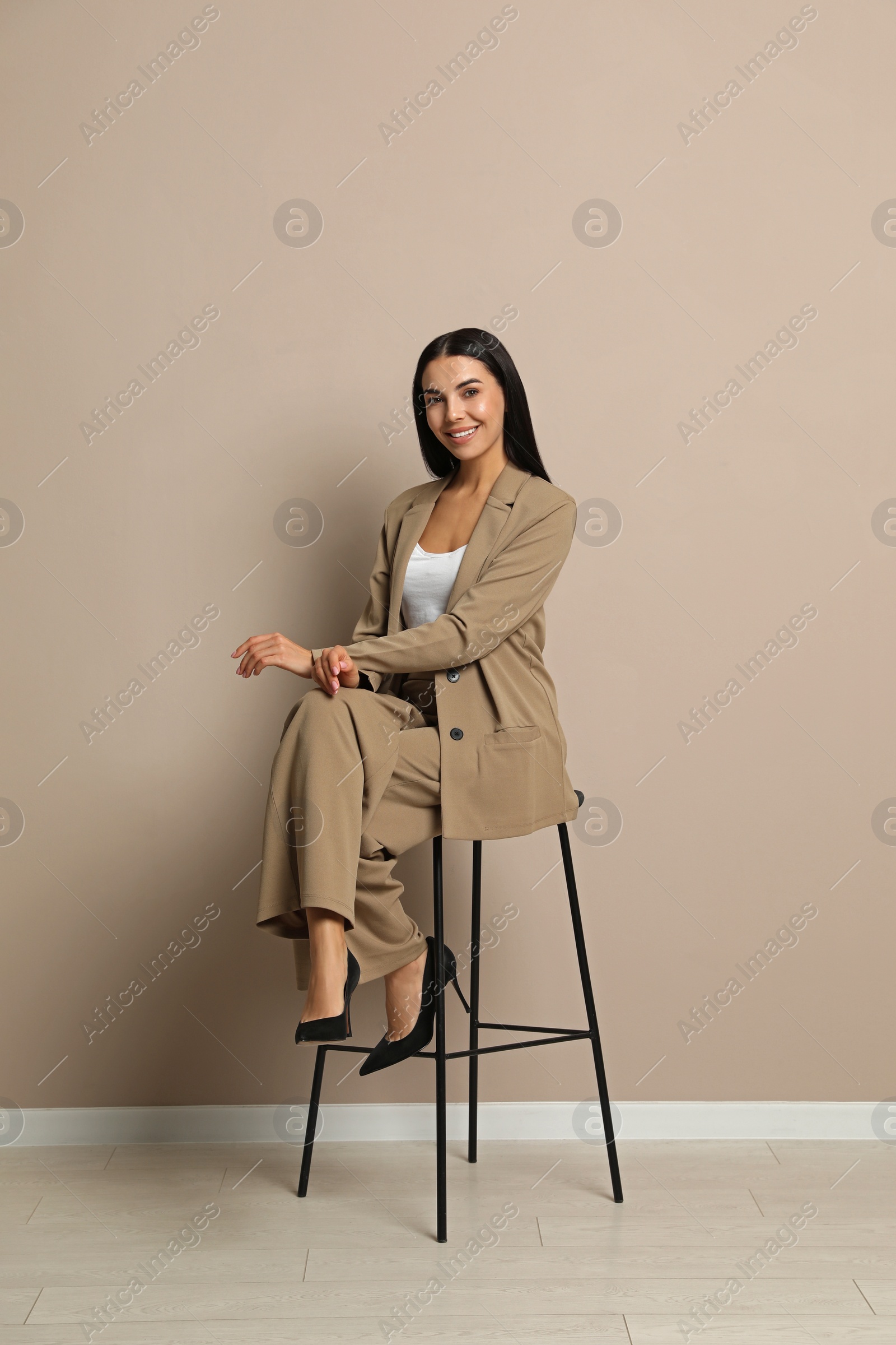 Photo of Beautiful young businesswoman sitting on stool near beige wall