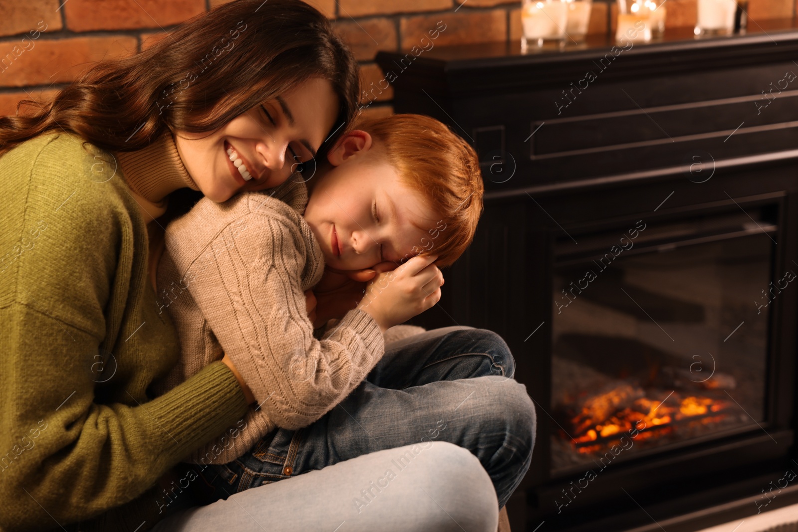 Photo of Happy mother and son hugging near fireplace at home