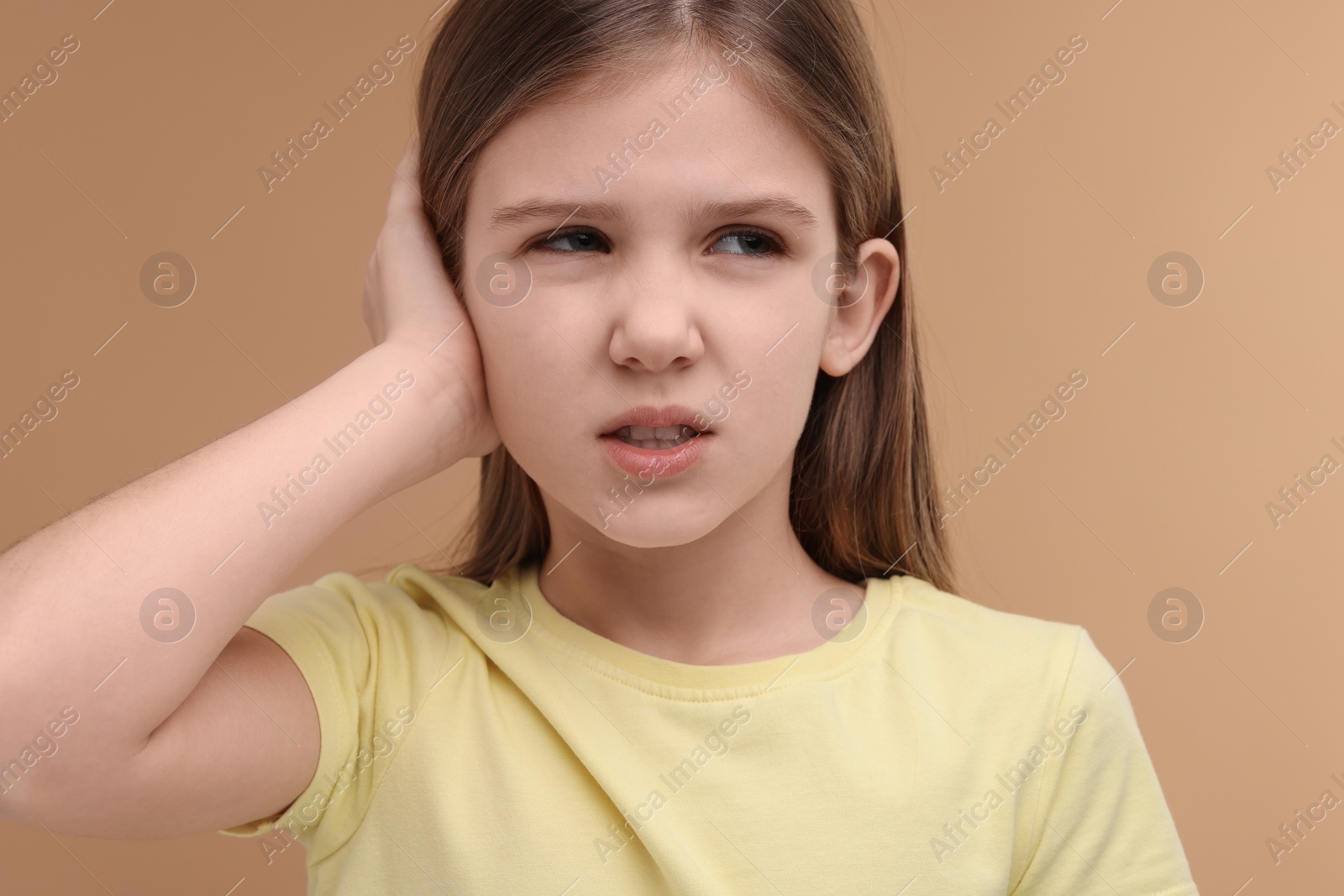 Photo of Hearing problem. Little girl suffering from ear pain on pale brown background