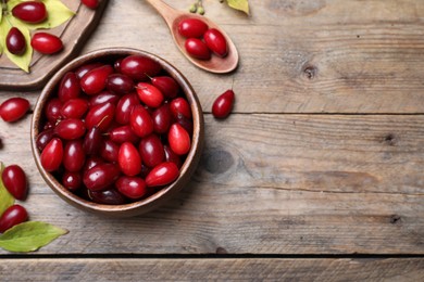 Photo of Fresh ripe dogwood berries with green leaves on wooden table, flat lay. Space for text