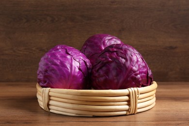 Photo of Wicker basket with fresh red cabbages on wooden table