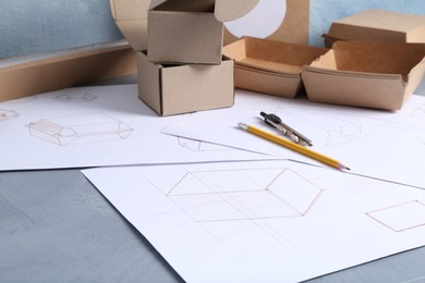 Photo of Creating packaging design. Drawings, boxes and stationery on blue textured table, closeup