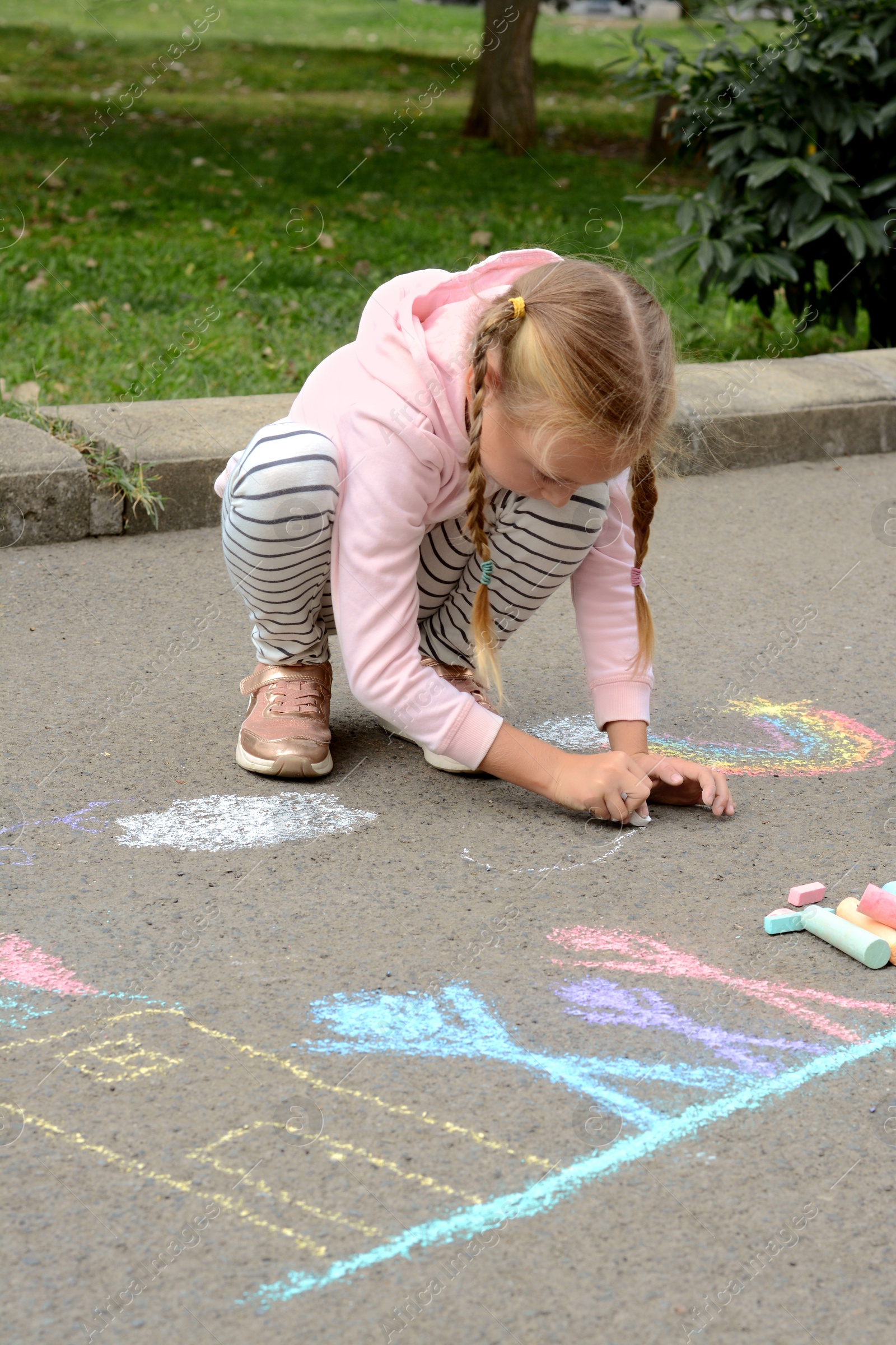 Photo of Little child drawing white clouds with chalk on asphalt