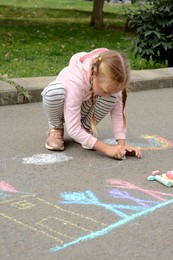 Photo of Little child drawing white clouds with chalk on asphalt