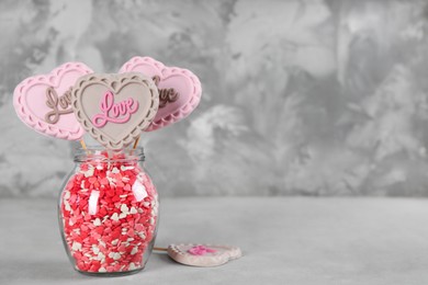 Heart shaped lollipops made of chocolate with sprinkles in glass on grey table, space for text