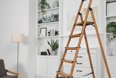 Photo of Wooden folding ladder near chest of drawers and shelves with accessories in room