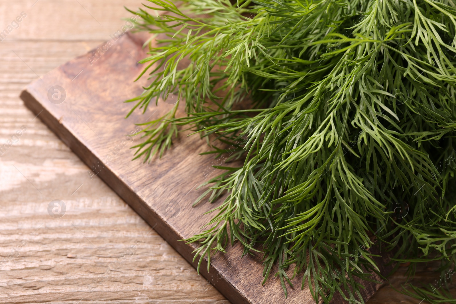 Photo of Board with sprigs of fresh dill on wooden table, closeup