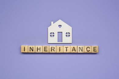 Photo of Word Inheritance made with wooden cubes and house model on color background, flat lay