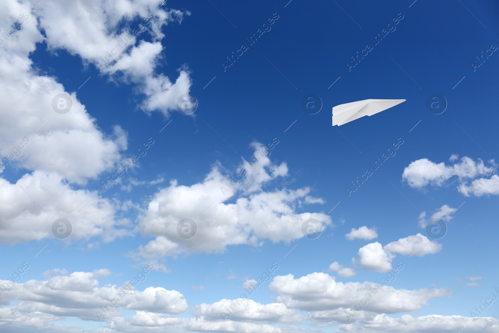 Image of White paper plane flying in blue sky with clouds