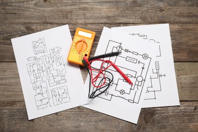 Wiring diagrams and digital multimeter on wooden table, flat lay