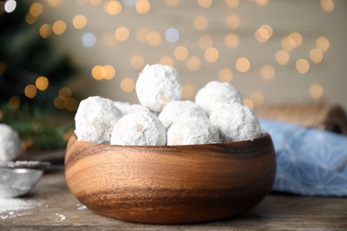 Tasty snowball cookies in wooden bowl against blurred festive lights. Christmas treat