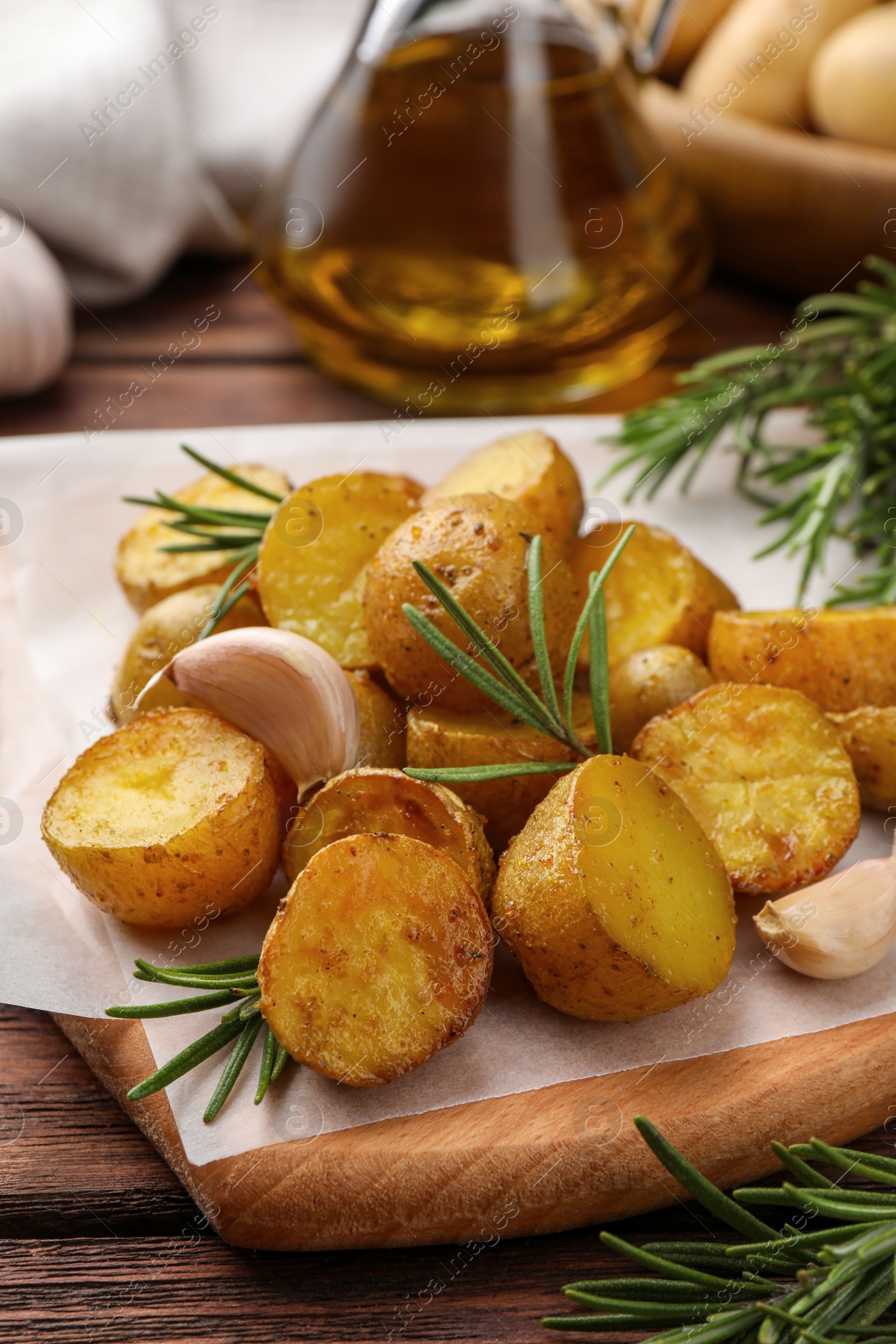 Photo of Delicious baked potatoes with rosemary and garlic on parchment paper, closeup