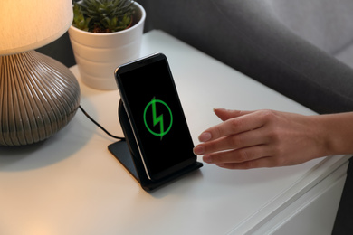 Photo of Woman taking smartphone from wireless charger in room, closeup